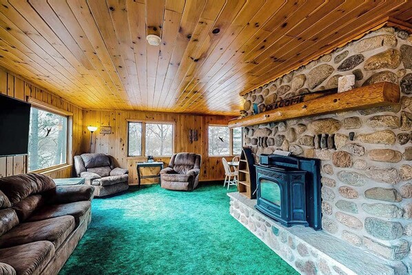 A log cabin interior with a stone fireplace, wooden walls, and a green carpet.