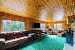 A log cabin interior with a large leather sofa, a fireplace, and a television.