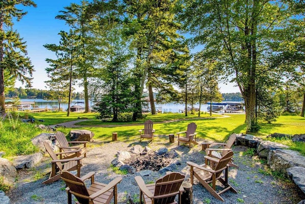 Un espacio al aire libre junto al lago con sillones Adirondack y un brasero.