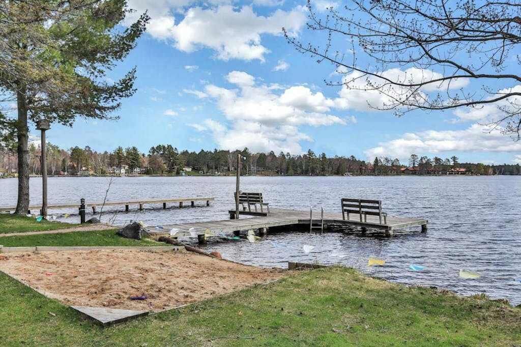 Un parco sul lago con un molo di legno, panchine e una spiaggia di sabbia.