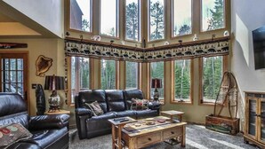 Una sala de estar acogedora con un sofá de cuero, una mesa de centro de madera y ventanas grandes con vistas a árboles.