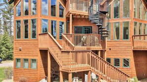 Una cabaña de madera de varios pisos con ventanas amplias, una escalera central y una escalera de caracol.