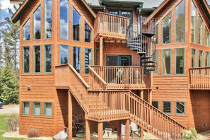 Una cabaña de madera de varios pisos con ventanas amplias, una escalera central y una escalera de caracol.