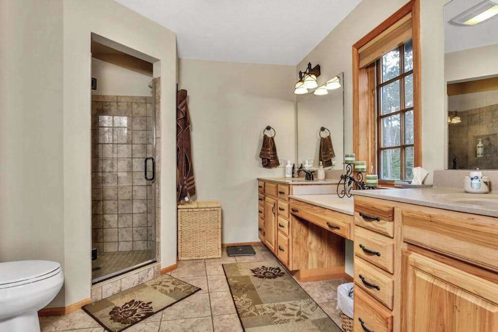 A bathroom with a shower, a toilet, wooden cabinets, a sink, and a large mirror.