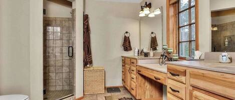 A bathroom with a shower, a toilet, wooden cabinets, a sink, and a large mirror.