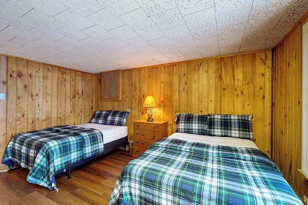 Een kamer met twee bedden, houten wanden, een plafond met ruitmotief en een nachtkastje met een lamp.