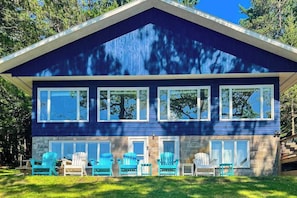 A two-story house with a steep gable roof, large windows, and a front porch with outdoor seating. - Lakefront Lodge w/ 2 additional cabins, private dock, firepit, kayak & hammock (Woodruff)