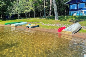 Una masa de agua cristalina con barcos, un sendero de piedra y una casa de color azul con ventanas.