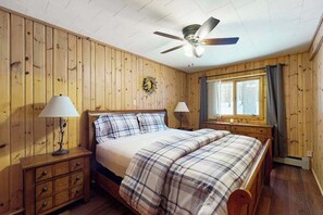 Ein Schlafzimmer mit Holzwänden, einem Bett, zwei Nachttischen, einem Deckenventilator und einem Fenster mit Vorhängen.