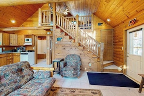 A cabin interior with a wooden staircase, a sofa, a chair, a small table, and a microwave in the kitchen area. - Cozy cabins w/ fireplace, whirlpool tub, access to private dock, & fire pit (Mercer)