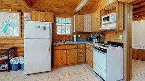 Een keukentje in chaletstijl met een koelkast, fornuis, magnetron en houten kastjes.