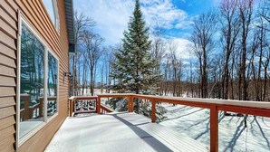 A wooden deck with a railing, snow-covered ground, and a large evergreen tree in the background. - Cozy Retreat, perfect for outdoor enthusiasts, near lakes, trails & downtown (Phelps)