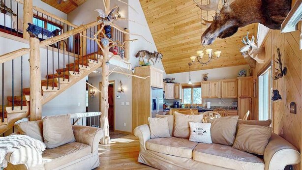 A spacious living area with a wooden staircase, a sofa set, and a kitchen in the background. - Cozy Retreat, perfect for outdoor enthusiasts, near lakes, trails & downtown (Phelps)