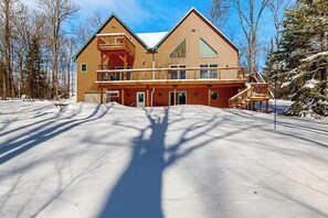 A two-story lodge with a balcony, a covered porch, and a snow-covered driveway.