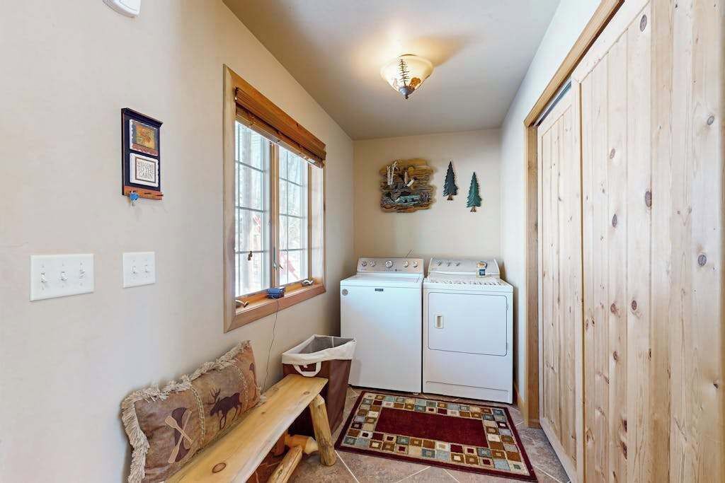 A laundry room with two washing machines, a bench, a rug, and a wall-mounted light fixture.