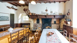 A traditional dining room with wooden furniture, a fireplace, and various kitchen utensils displayed on shelves. - Gîte le Caddet – Traditional Béarnais Farmhouse for Groups and Families (Poursiugues-Boucoue)