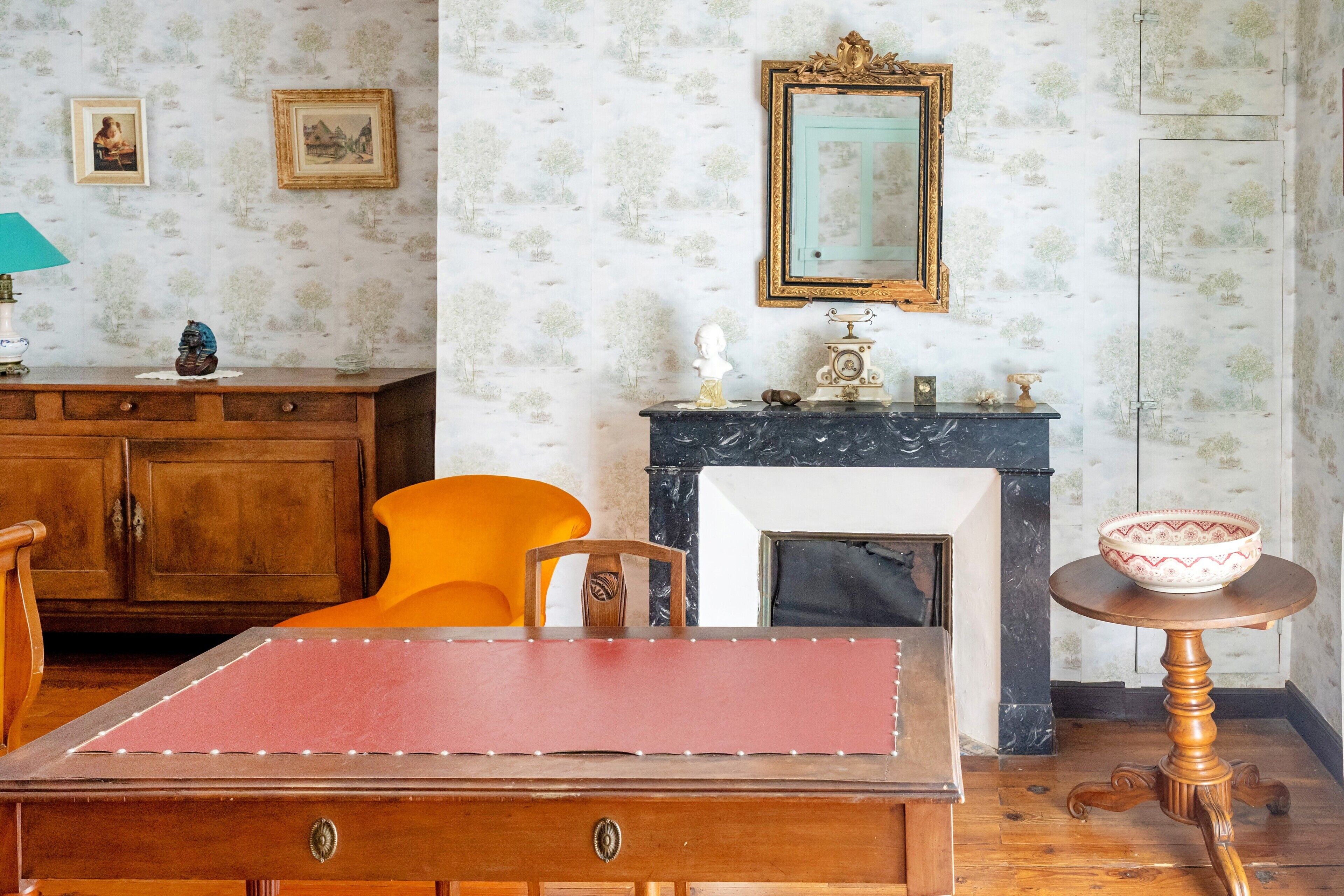 Een kamer met een houten kast, een rode tafel, een open haard en een muur met ingelijste foto's.
