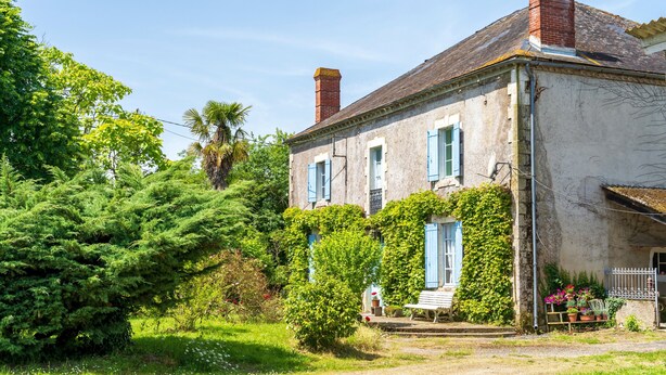 A two-story house with a brick chimney, ivy-covered walls, and a bench outside. - Gîte le Caddet – Traditional Béarnais Farmhouse for Groups and Families (Poursiugues-Boucoue)