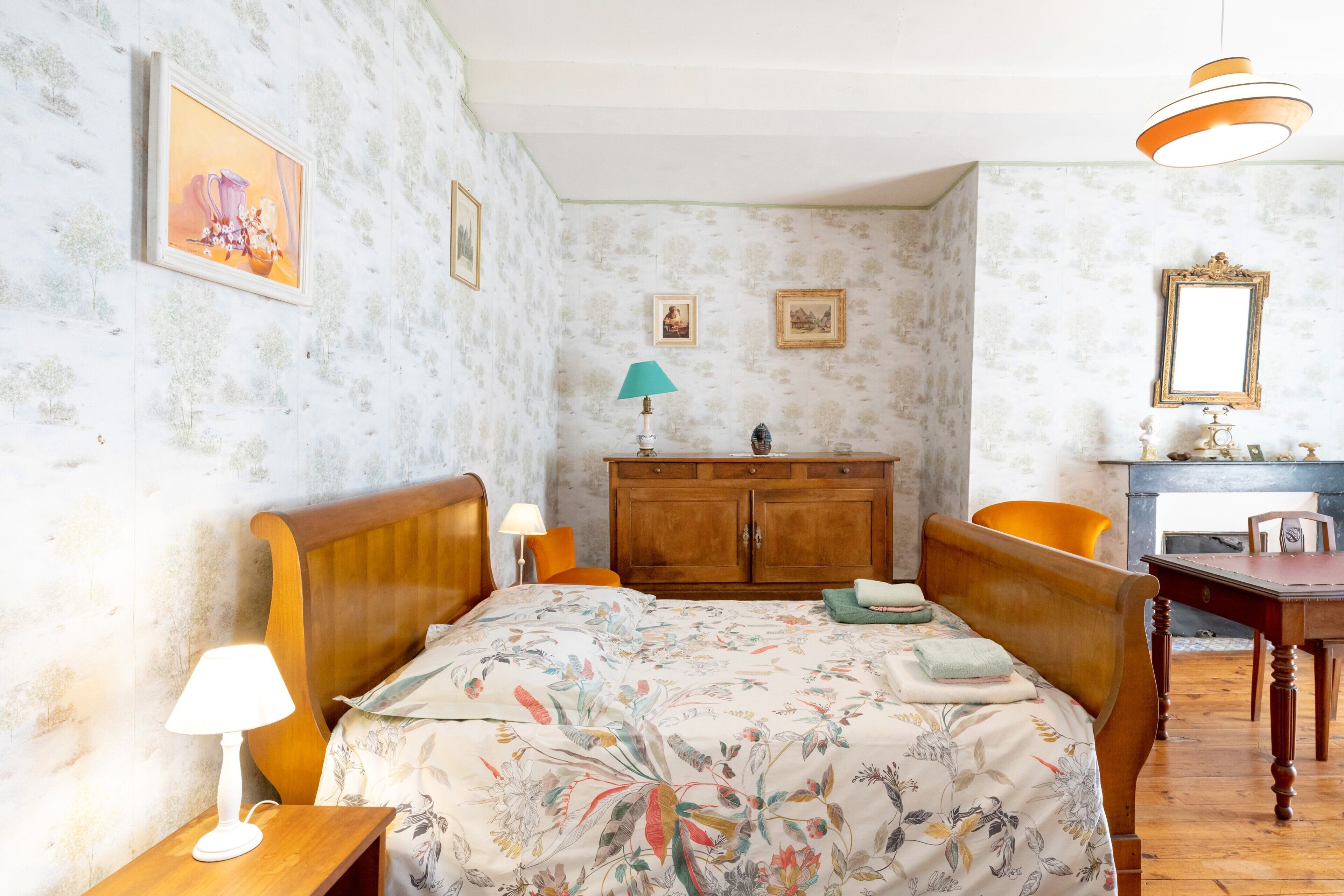 A bedroom with a wooden bed, a nightstand, a desk, a chair, a dresser, and a mirror.
