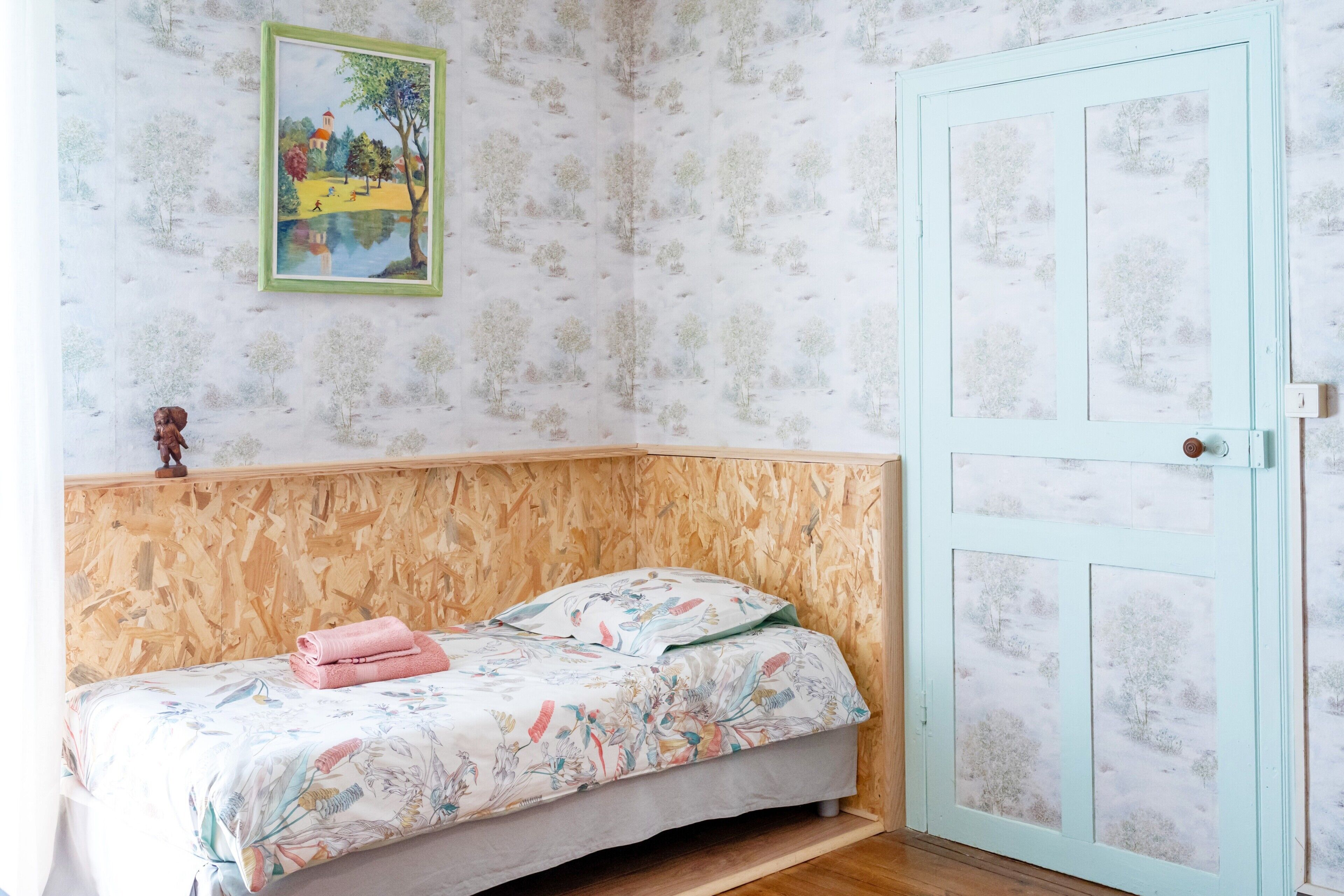 Une pièce avec un lit, une porte et un mur recouvert d’un papier peint à motifs.