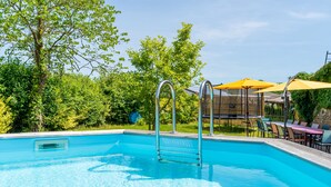 A clear swimming pool with a metal ladder, surrounded by lush greenery and outdoor furniture. - Gîte le Caddet – Traditional Béarnais Farmhouse for Groups and Families (Poursiugues-Boucoue)
