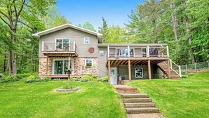 Ein zweigeschossiges Haus mit einer Veranda, einem Steinfundament und einer Holztreppe, die zur Veranda führt.
