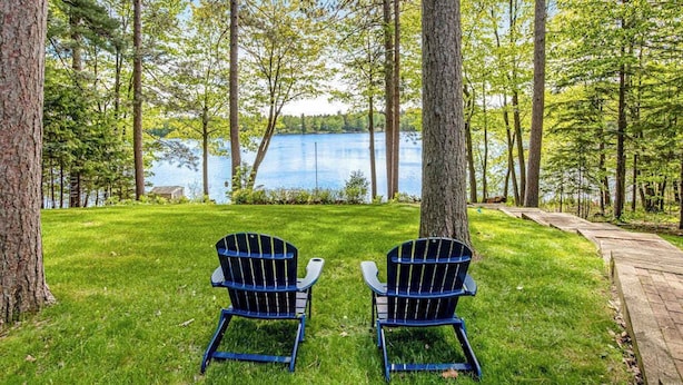 Zwei Adirondack-Stühle vor einem von Bäumen gesäumten See.
