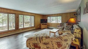 Una sala de estar con sofá, mesa de centro, televisor y ventanas amplias.