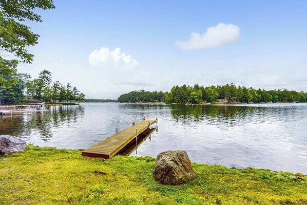 A calm lake with a wooden dock extending into the water, surrounded by grassy areas and trees.