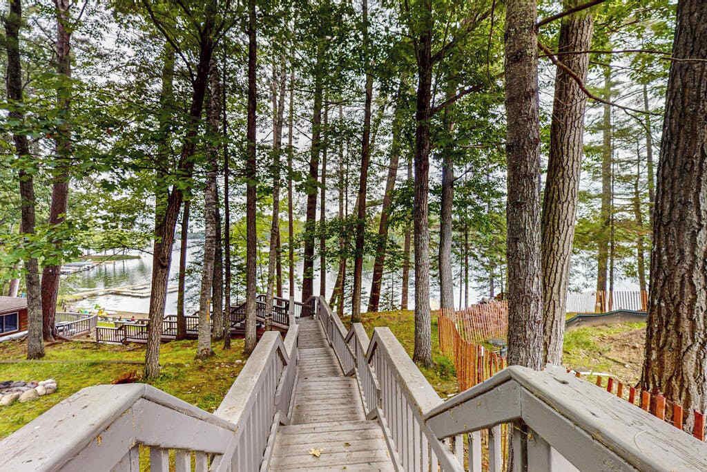 Un escalier en bois menant à une jetée, entouré de grands arbres et bordé par un lac.