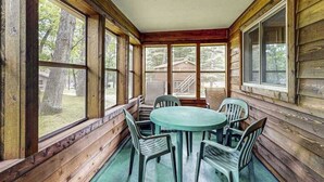 Una cabaña de madera con un porche, una mesa redonda y cuatro sillas.