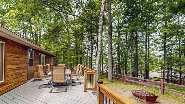 Una terraza de madera con mobiliario exterior, rodeada de un bosque.