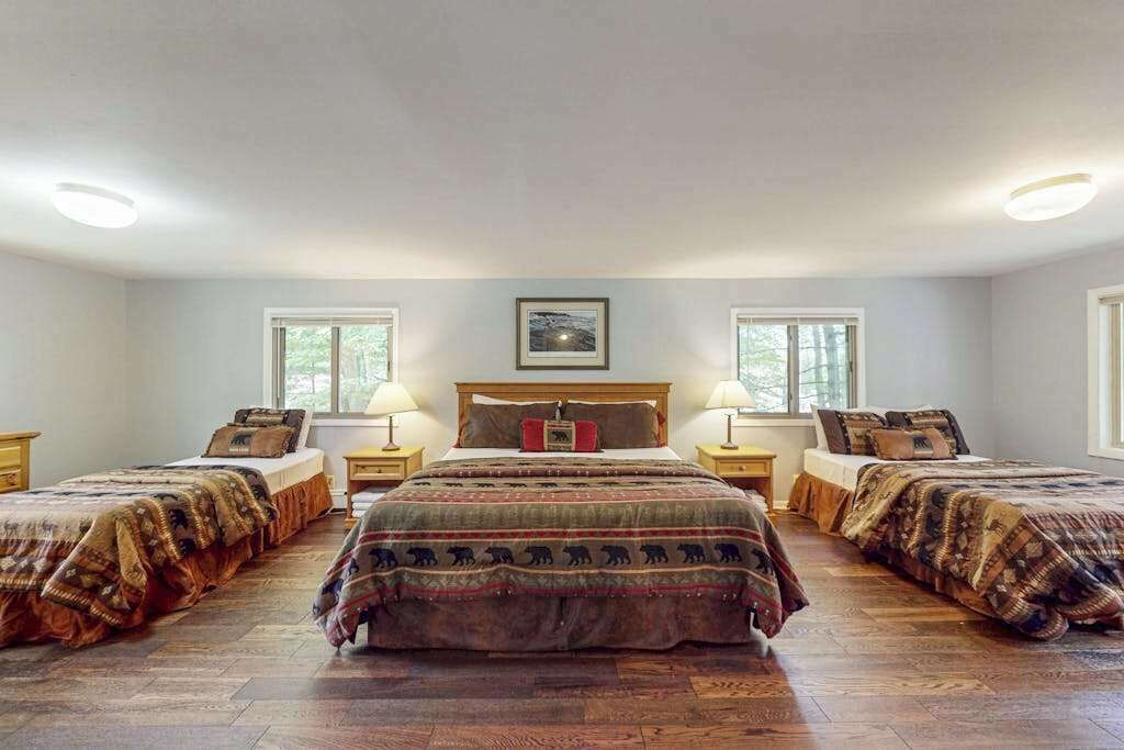 Ein Zimmer mit zwei Betten, einem Holzkopfstück, Nachttischen mit Lampen und einem gerahmten Bild an der Wand.