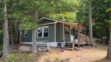Une cabane dotée d’une véranda, entourée d’arbres.