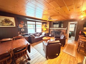 A cozy cabin interior with a wooden ceiling, a fireplace, a sofa, a dining table, and a bar area. - Blue Jay Cabin | Lakefront cabin in Rhinelander with dock & row boat (Rhinelander)
