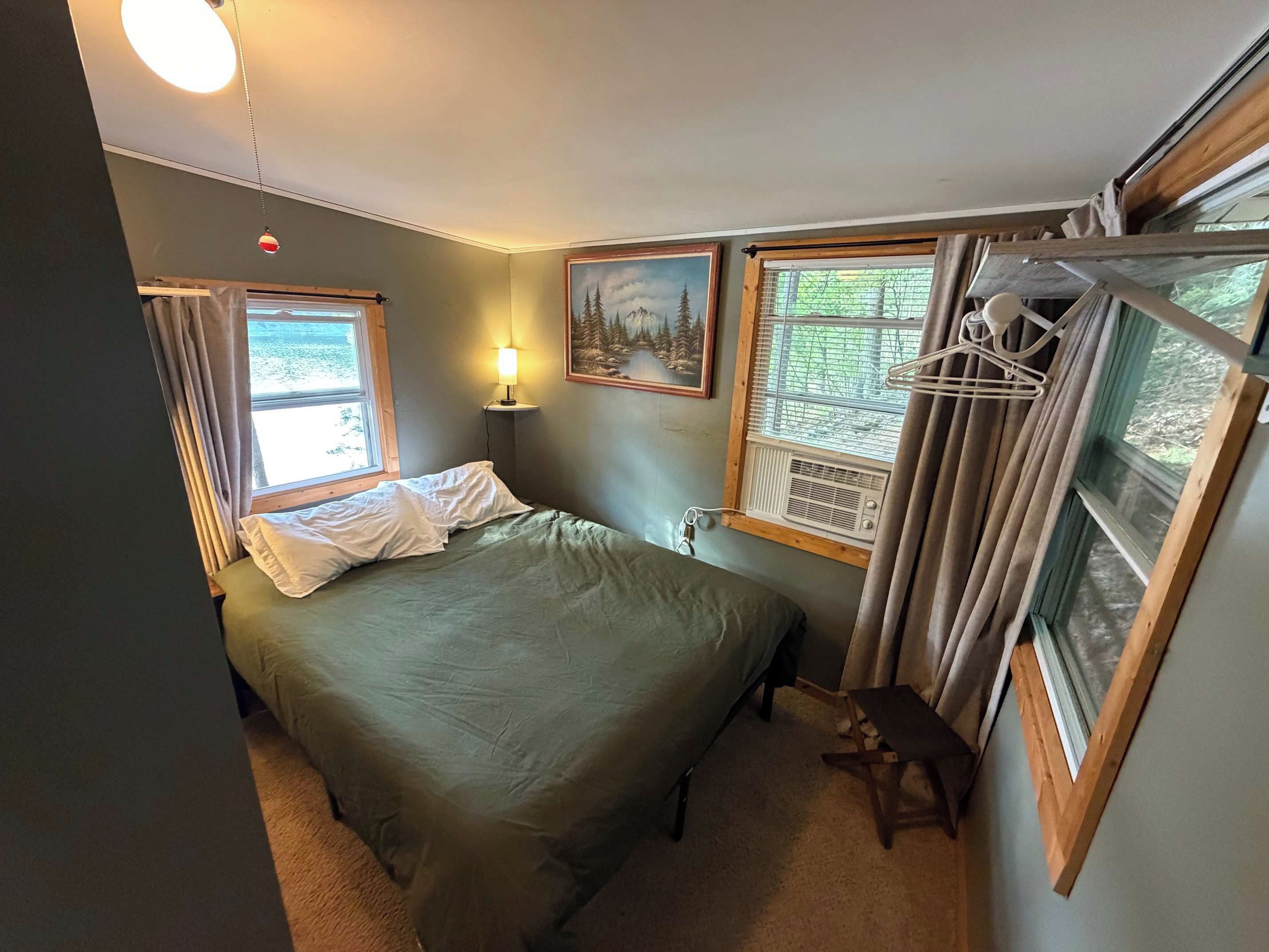 Une chambre à coucher avec un lit, une lampe de chevet, une fenêtre avec des rideaux et un tableau au mur.