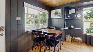 A dining area with a wooden table and chairs, a window with blinds, and a shelf with books and a lamp. - Blue Jay Cabin | Lakefront cabin in Rhinelander with dock & row boat (Rhinelander)