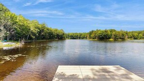 A calm lake with a wooden dock extending into the water, surrounded by dense green trees. - Blue Jay Cabin | Lakefront cabin in Rhinelander with dock & row boat (Rhinelander)