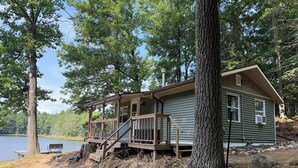 A cabin with a deck, a bench, and a view of a lake. - Blue Jay Cabin | Lakefront cabin in Rhinelander with dock & row boat (Rhinelander)