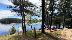 Un terrain de camping au bord du lac, avec un quai, des chaises Adirondack rouges et une table de pique-nique.