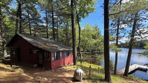 Une cabane avec un quai s’avançant dans un lac, entourée de grands arbres.