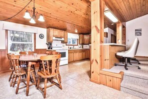 Un intérieur en bois comprenant une table à manger, des chaises, un coin cuisine et une chaise de bureau blanche.