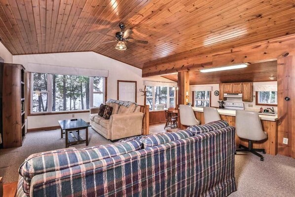 L’intérieur chaleureux d’un chalet avec un plafond en bois, un canapé, une table à manger et un coin cuisine.