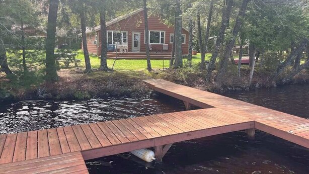 Una cabaña con un muelle que se adentra en un estanque, rodeada de árboles.