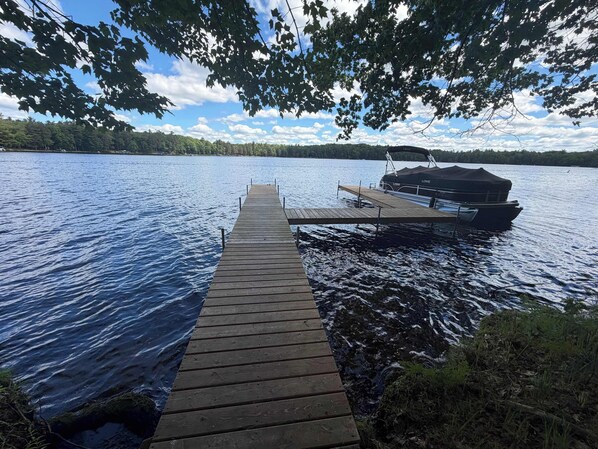 A wooden dock extending into a lake with a boat docked on the right.