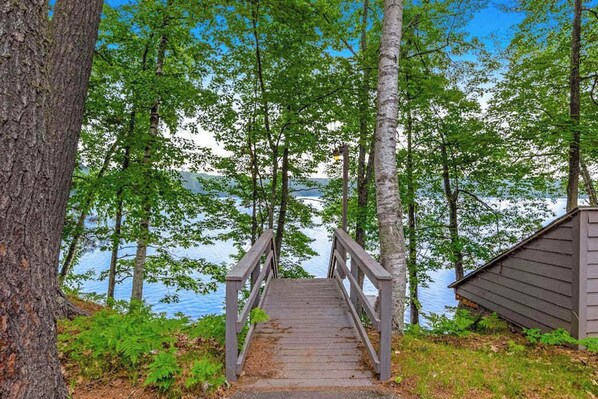 A wooden bridge leading to a dock by a lake, surrounded by trees. - Snowy lake-view cabin with fireplace, full kitchen, TV, dock, & DVD player (St. Germain)