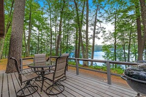 A wooden deck with outdoor furniture, overlooking a lake surrounded by trees. - Snowy lake-view cabin with fireplace, full kitchen, TV, dock, & DVD player (St. Germain)