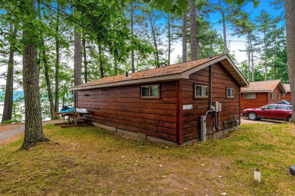 A wooden cabin with a sloped roof, a small porch, and a visible water spigot.