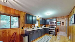 Une cuisine avec des meubles en bois, un four à micro-ondes, un four traditionnel, un réfrigérateur et une fenêtre donnant sur les arbres.