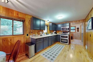 A kitchen with wooden cabinets, a microwave, an oven, a refrigerator, and a window with a view of trees. - North Twin Lake Cabin w/ kayak, paddle boards, dock, gas grill, fire pit & WIFI (Phelps)
